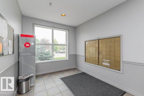 Bright, welcoming entryway featuring large windows with natural light, ceramic tile flooring, a charcoal entry mat, wall-mounted mailboxes with brass-finish hardware, and recessed ceiling lighting - #208 10421 42 Av Nw, Edmonton, AB - Indoor Photo Showing Other Room