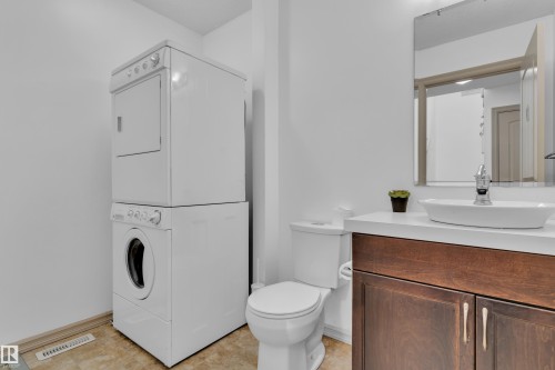 Compact bathroom featuring a contemporary wood-finish vanity with a vessel sink, a wall-mounted mirror, and a white toilet - 7223 19A Avenue Sw, Edmonton, AB - Indoor Photo Showing Laundry Room