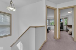 Upper-level hallway featuring light wood-finish trim, white walls, and neutral carpet flooring - 