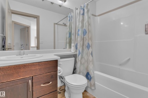 Bathroom featuring a wood-finish vanity with an integrated sink, a white countertop, and a shower-over-tub combination with a grab bar - 7223 19A Avenue Sw, Edmonton, AB - Indoor Photo Showing Bathroom