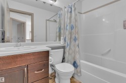 Bathroom featuring a wood-finish vanity with an integrated sink, a white countertop, and a shower-over-tub combination with a grab bar - 