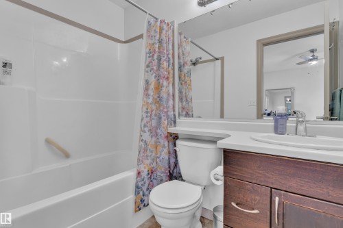 Bathroom featuring a white tub/shower combination with a grab bar, a single-flush toilet, a wood-finish vanity with cabinet storage, a white countertop, and an integrated sink with a chrome faucet - 7223 19A Avenue Sw, Edmonton, AB - Indoor Photo Showing Bathroom