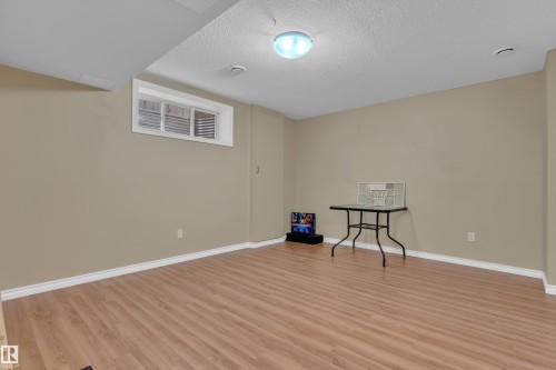 Lower-level room featuring wood-finish flooring, neutral wall tones, white baseboards, a single egress window, and a flush-mount ceiling light fixture - 7223 19A Avenue Sw, Edmonton, AB - Indoor Photo Showing Other Room