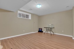 Lower-level room featuring wood-finish flooring, neutral wall tones, white baseboards, a single egress window, and a flush-mount ceiling light fixture - 