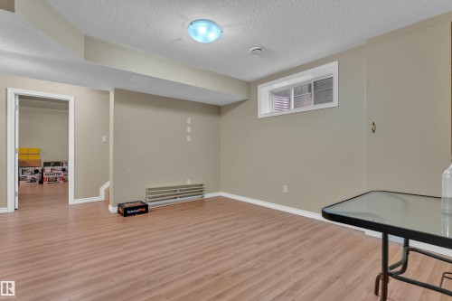 Spacious lower-level room featuring wood-finish flooring, neutral wall paint, white baseboards, and a single window - 7223 19A Avenue Sw, Edmonton, AB - Indoor Photo Showing Other Room