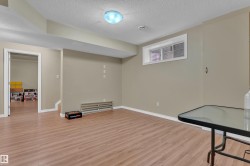 Spacious lower-level room featuring wood-finish flooring, neutral wall paint, white baseboards, and a single window - 