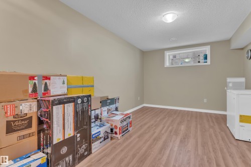Spacious lower-level room featuring wood-finish flooring, neutral wall paint, and white baseboards - 7223 19A Avenue Sw, Edmonton, AB - Indoor