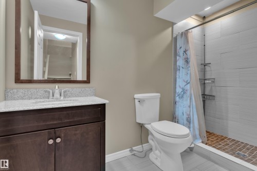 Bathroom featuring a dark wood vanity with a light-toned countertop, a shower with horizontal tile walls, and a tiled shower pan - 7223 19A Avenue Sw, Edmonton, AB - Indoor Photo Showing Bathroom