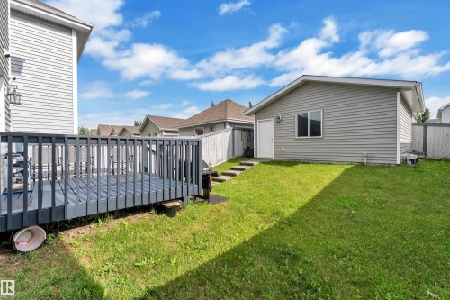 Private backyard featuring a gray wooden deck, a separate structure with gray siding and a window, a white rear entry door, and a manicured lawn - 7223 19A Avenue Sw, Edmonton, AB - Outdoor