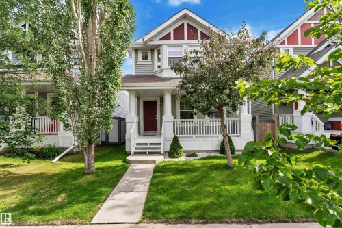 Modern façade featuring grey siding with red trim accents, a welcoming front porch with white railings, a contrasting red front door, and a manicured lawn with established trees - 7223 19A Avenue Sw, Edmonton, AB - Outdoor With Facade