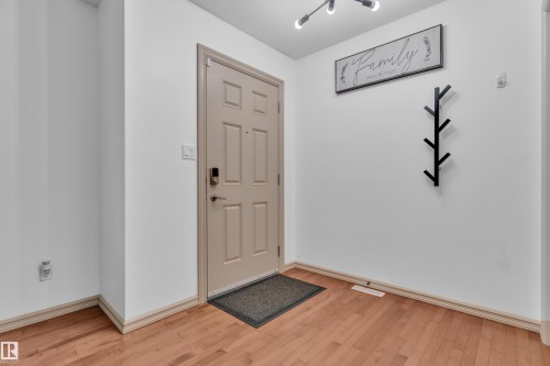 Entryway featuring a panel door with smart lock hardware, light wood-finish flooring, white walls, and a modern track lighting fixture - 7223 19A Avenue Sw, Edmonton, AB - Indoor Photo Showing Other Room