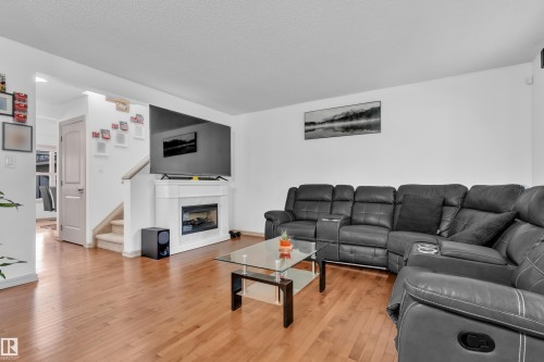 Living area featuring wood-finish flooring, a white-mantled fireplace, and a partial staircase with carpeted treads - 7223 19A Avenue Sw, Edmonton, AB - Indoor Photo Showing Living Room With Fireplace
