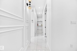 Hallway featuring white wainscoting, polished tile flooring, recessed lighting, and a modern sconce fixture - 