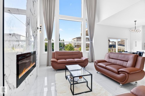 Living area featuring high ceilings, tall windows with drapes, a white marble-patterned fireplace with a built-in electric insert, and glossy white tile flooring - 3926 41 Avenue, Beaumont, AB - Indoor Photo Showing Living Room With Fireplace