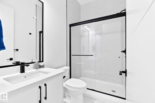 Contemporary bathroom featuring a frameless glass shower enclosure with matte black hardware, a white vanity with integrated sink and storage, and a large wall mirror - 3926 41 Avenue, Beaumont, AB - Indoor Photo Showing Bathroom