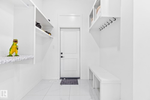 Mudroom featuring white built-in shelving, a full-height solid panel door with dark hardware, a built-in bench, and white tile flooring - 3926 41 Avenue, Beaumont, AB - Indoor With Storage