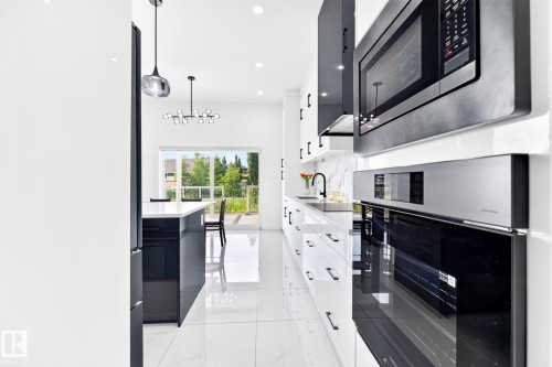 Gourmet kitchen featuring high-gloss white cabinetry, a large kitchen island with counter seating, built-in stainless steel appliances, a white tile backsplash, and oversized white tile flooring - 3926 41 Avenue, Beaumont, AB - Indoor