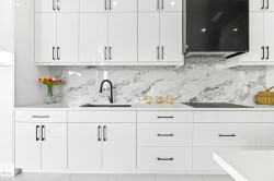 Modern kitchen featuring white high-gloss cabinetry with black hardware, a black kitchen faucet, and a black range hood - 