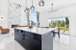 Spacious open-concept interior featuring a substantial kitchen island with a white countertop and dark cabinetry, a floor-to-ceiling accent wall with a linear fireplace, and large windows - 