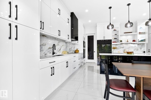 Modern kitchen featuring high-gloss white cabinetry with matte black hardware, a marble-patterned backsplash, and polished white floor tiles - 3926 41 Avenue, Beaumont, AB - Indoor