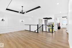 Spacious interior featuring wood-finish flooring, wainscoting accent wall, a tray ceiling with a modern chandelier, and a glass-paneled railing - 
