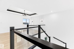 Open concept upper landing featuring a black metal and glass railing, contemporary chandelier, recessed ceiling tray, and decorative wall paneling - 