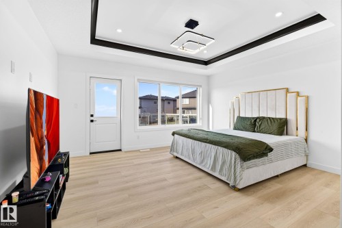 Spacious room featuring light wood-finish flooring, a contemporary tray ceiling with recessed lighting and a modern square light fixture, and large windows providing abundant natural light - 3926 41 Avenue, Beaumont, AB - Indoor Photo Showing Bedroom