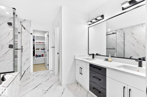 Modern bathroom featuring a double vanity with white cabinetry, matte black hardware, and an expansive mirror - 3926 41 Avenue, Beaumont, AB - Indoor Photo Showing Bathroom