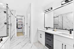 Modern bathroom featuring a double vanity with white cabinetry, matte black hardware, and an expansive mirror - 