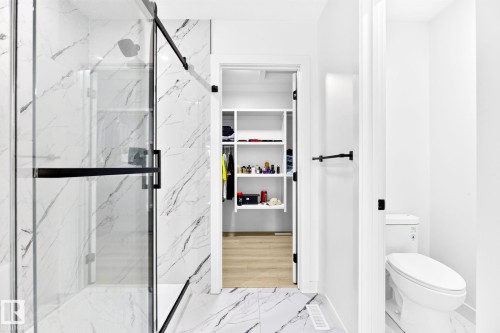Contemporary bathroom featuring a spacious glass-enclosed shower with black fixtures and marble-finish tile, coordinated marble-finish flooring, and a separate water closet - 3926 41 Avenue, Beaumont, AB - Indoor Photo Showing Bathroom