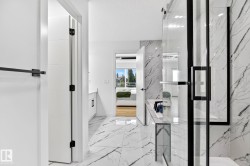 Bathroom featuring large format marble-look tile flooring and shower surround, a glass-enclosed shower with black trim, and white vanity cabinetry with a light-colored countertop - 