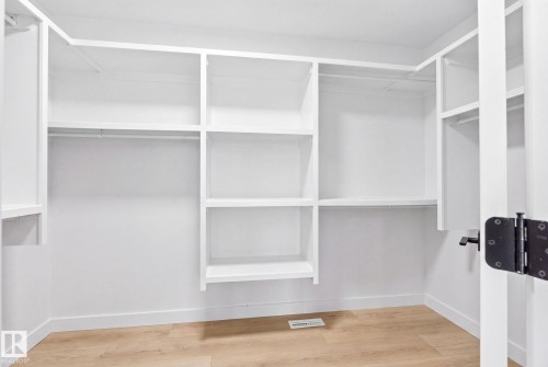 White walk-in closet featuring built-in shelving, multiple hanging rods, and wood-finish flooring - 3926 41 Avenue, Beaumont, AB - Indoor With Storage