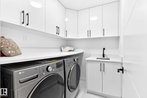 Dedicated utility area featuring white cabinetry with black hardware, white countertops, built-in sink with black faucet, and overhead lighting - 3926 41 Avenue, Beaumont, AB - Indoor Photo Showing Laundry Room