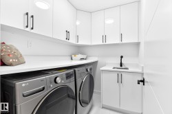 Dedicated utility area featuring white cabinetry with black hardware, white countertops, built-in sink with black faucet, and overhead lighting - 