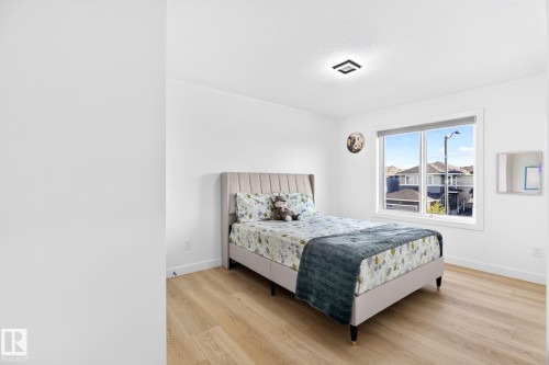 Bedroom featuring wood-finish flooring, a contemporary light fixture, and a large window with white trim - 3926 41 Avenue, Beaumont, AB - Indoor Photo Showing Bedroom