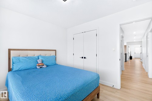 Bedroom featuring light wood-finish flooring, white walls, and a built-in double-door closet with matte black hardware - 3926 41 Avenue, Beaumont, AB - Indoor Photo Showing Bedroom