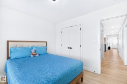 Bedroom featuring light wood-finish flooring, white walls, and a built-in double-door closet with matte black hardware - 
