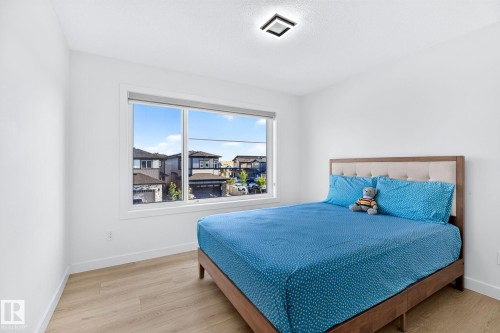 Bright room featuring a large window, light wood-finish flooring, white walls, a contemporary ceiling light fixture, and white baseboards - 3926 41 Avenue, Beaumont, AB - Indoor Photo Showing Bedroom