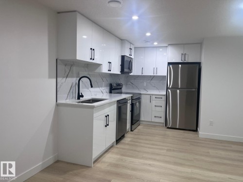 Modern kitchen featuring white high-gloss cabinetry with matte black hardware, stainless steel appliances, and wood-finish flooring - 3926 41 Avenue, Beaumont, AB - Indoor Photo Showing Kitchen