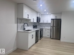 Modern kitchen featuring white high-gloss cabinetry with matte black hardware, stainless steel appliances, and wood-finish flooring - 