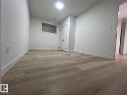 Spacious room featuring wood-finish flooring, crisp white walls, and bright overhead lighting - 