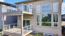 Rear exterior featuring two levels of outdoor living spaces, including a ground-level patio and an upper-level balcony, both with glass panel railings - 