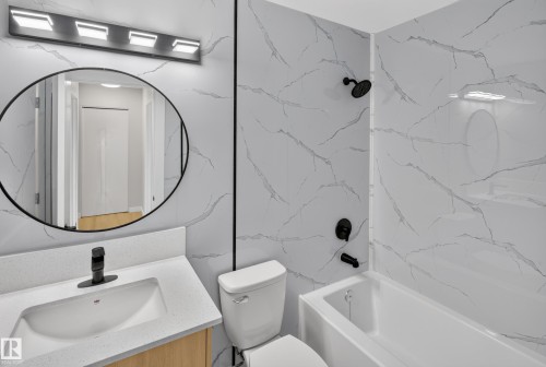 Modern bathroom featuring marble-look wall tile, a circular framed mirror with integrated lighting, white porcelain vanity with single-handle faucet, white toilet, and a bathtub with matte black fixtures and overhead showerhead - 175 Centennial Crest Nw, Edmonton, AB - Indoor