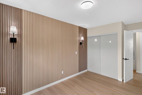 Spacious bedroom featuring warm wood-finish flooring, vertical shiplap accent wall with integrated sconces, and abundant natural light from recessed ceiling fixture - 175 Centennial Crest Nw, Edmonton, AB - Indoor Photo Showing Other Room