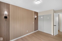 Spacious bedroom featuring warm wood-finish flooring, vertical shiplap accent wall with integrated sconces, and abundant natural light from recessed ceiling fixture - 