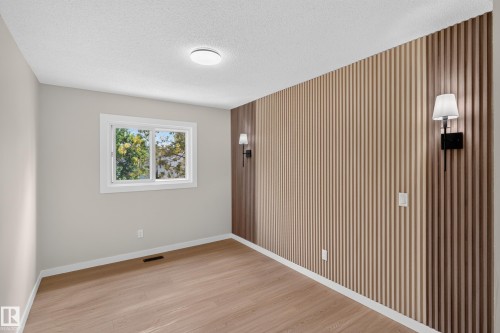 Bright bedroom showcasing wood-finish flooring, a large double-hung window with natural light, vertical shiplap accent wall with integrated wall sconce lighting, recessed ceiling fixture, and fresh neutral wall finishes - 175 Centennial Crest Nw, Edmonton, AB - Indoor Photo Showing Other Room