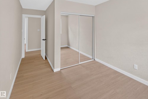 Spacious bedroom with wood-finish flooring, mirrored sliding closet doors, and neutral wall finishes - 175 Centennial Crest Nw, Edmonton, AB - Indoor Photo Showing Other Room