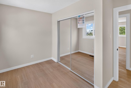 Spacious bedroom with wood-finish flooring, mirrored sliding closet doors with aluminum framing, and abundant natural light from a corner window - 175 Centennial Crest Nw, Edmonton, AB - Indoor Photo Showing Other Room