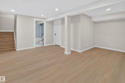 Spacious open-concept basement featuring warm wood-finish flooring throughout, recessed ceiling lighting, and support columns - 