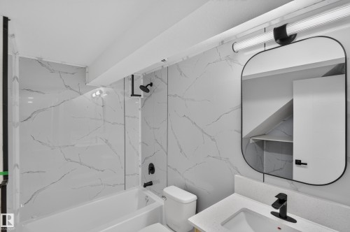Bathtub with black hardware and marble-patterned wall surfacing - 175 Centennial Crest Nw, Edmonton, AB - Indoor Photo Showing Bathroom